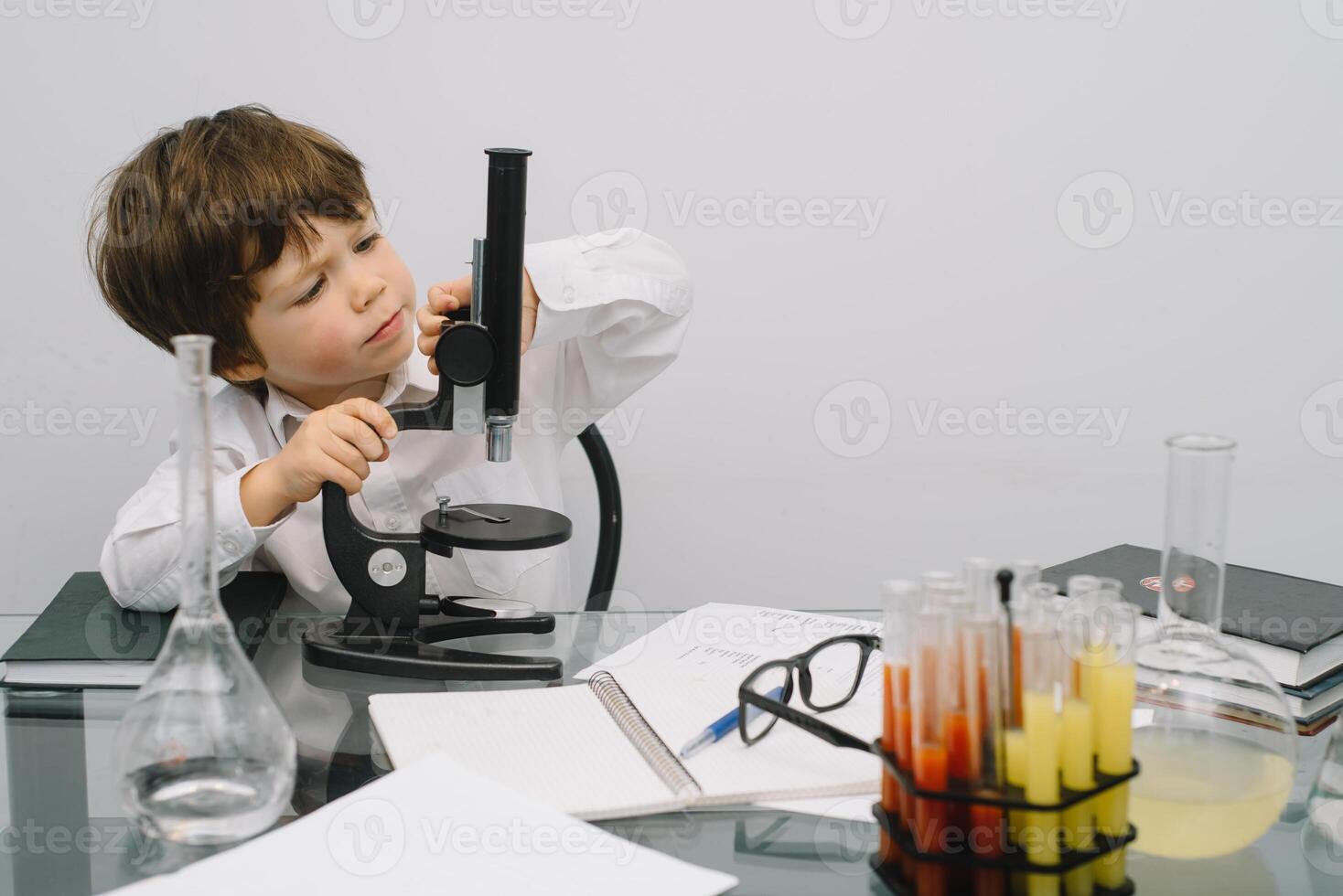 The boy with a microscope and various colorful flasks on a white background. A boy doing experiments in the laboratory. Explosion in the laboratory. Science and education photo