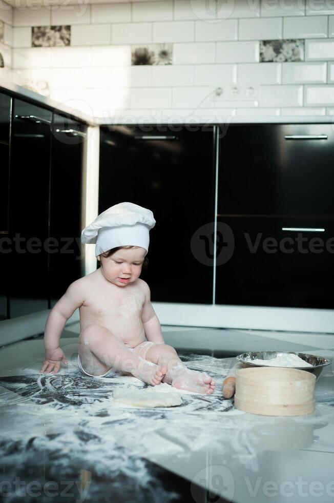 pequeño chico sentado en alfombra en cocina jugando con Cocinando ollas. linda chico Cocinando en cocina a hogar foto