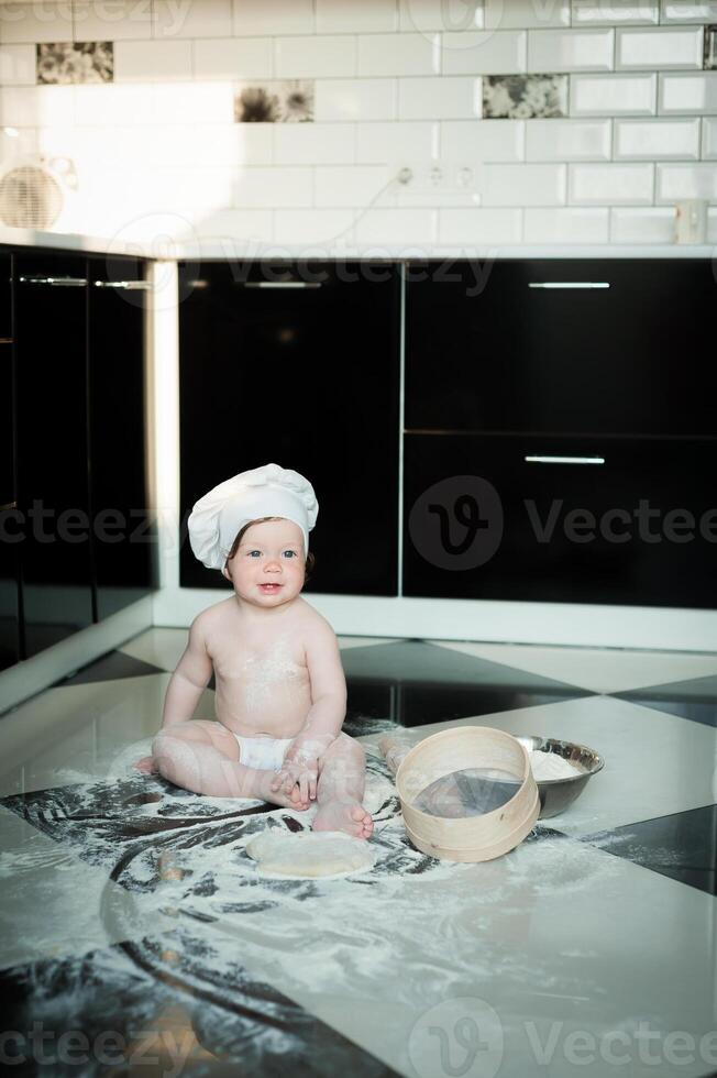 Little boy sitting on carpet in kitchen playing with cooking pots. Cute boy cooking in kitchen at home photo