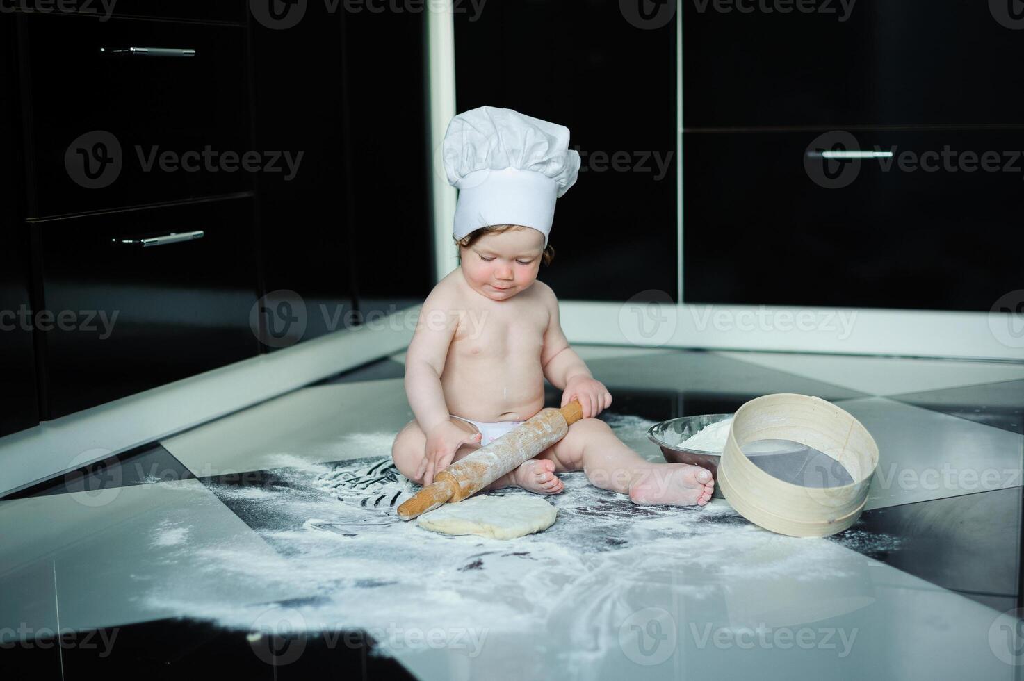 Little boy sitting on carpet in kitchen playing with cooking pots. Cute boy cooking in kitchen at home photo