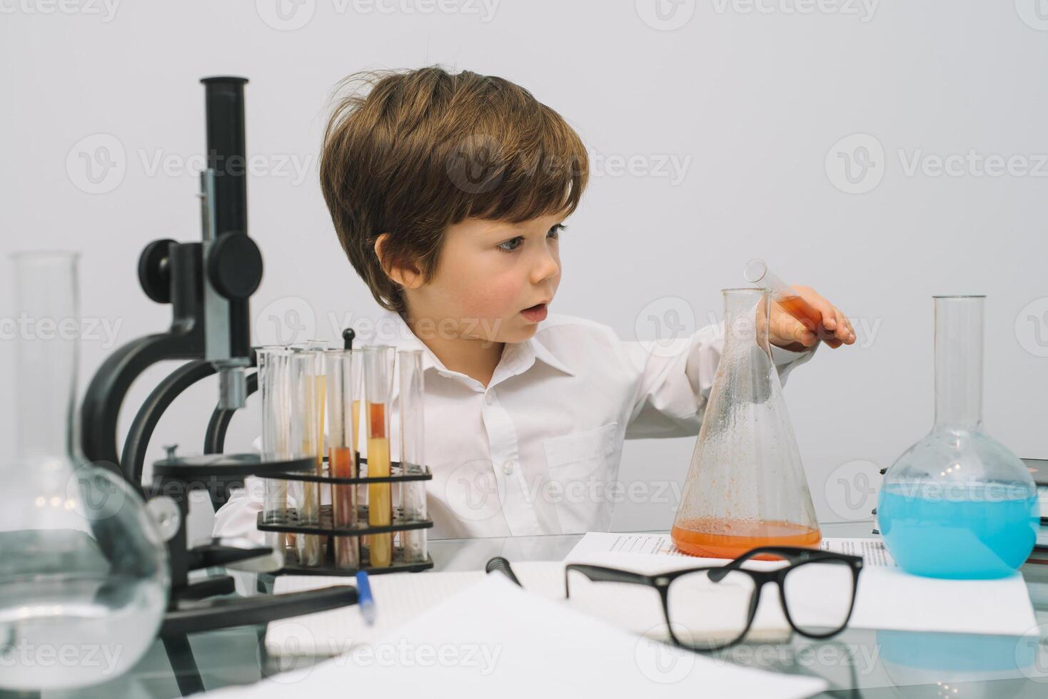 The boy with a microscope and various colorful flasks on a white background. A boy doing experiments in the laboratory. Explosion in the laboratory. Science and education photo