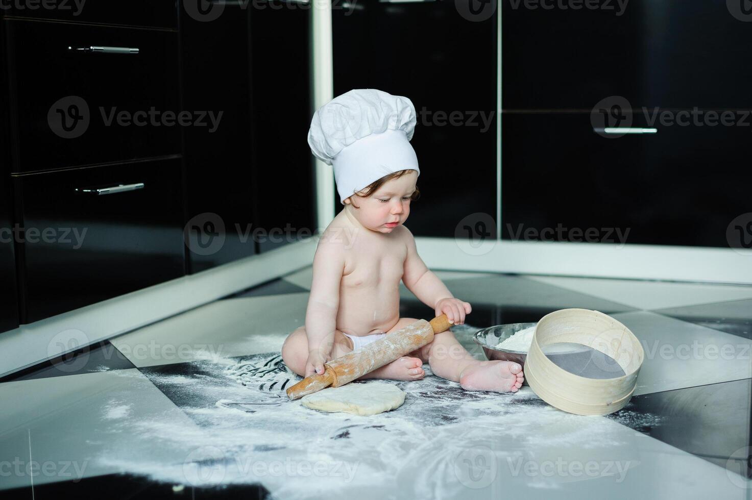 Little boy sitting on carpet in kitchen playing with cooking pots. Cute boy cooking in kitchen at home photo