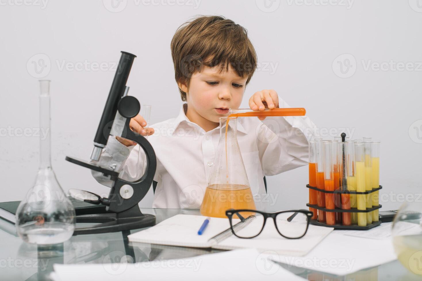 The boy with a microscope and various colorful flasks on a white background. A boy doing experiments in the laboratory. Explosion in the laboratory. Science and education photo