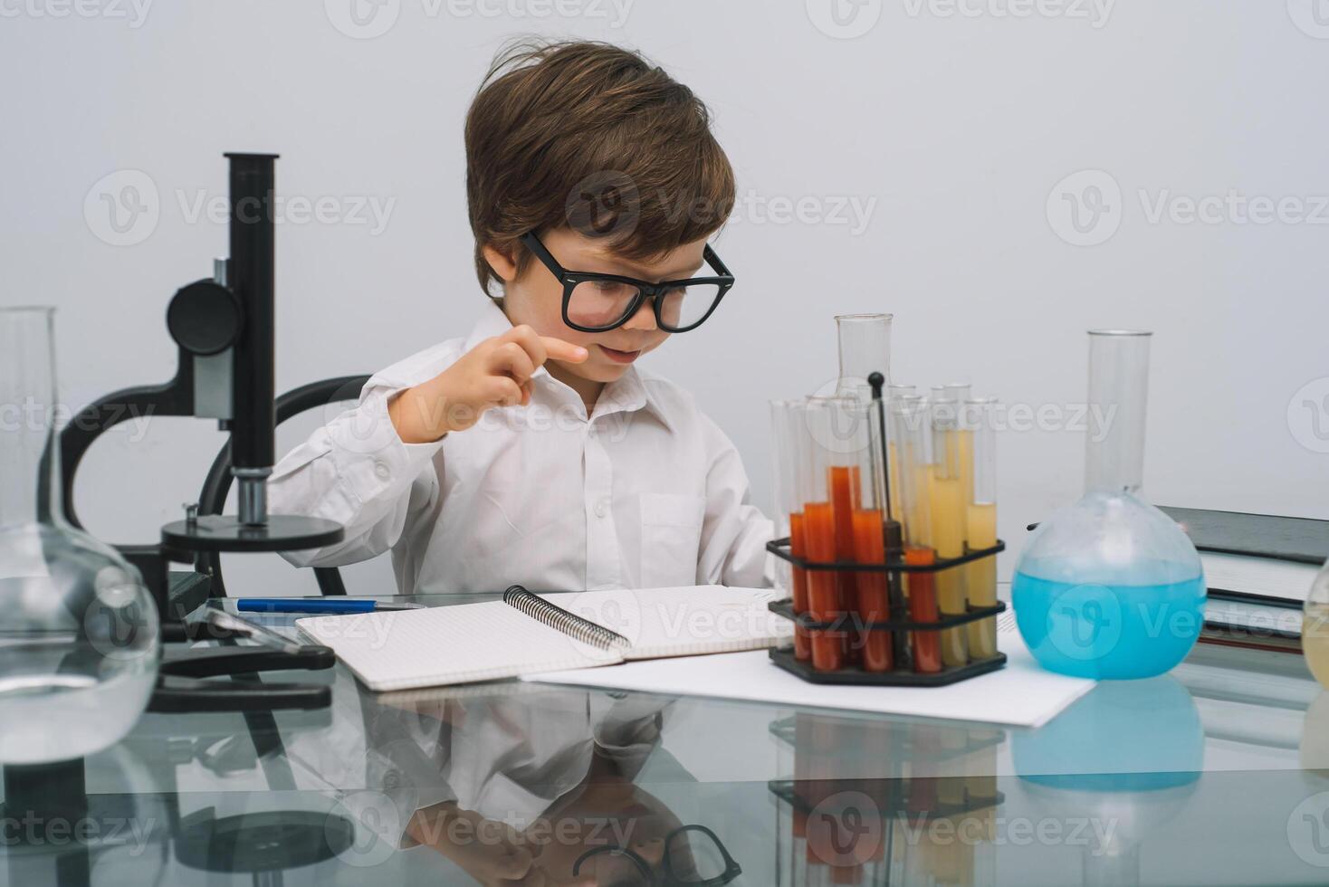 The boy with a microscope and various colorful flasks on a white background. A boy doing experiments in the laboratory. Explosion in the laboratory. Science and education photo