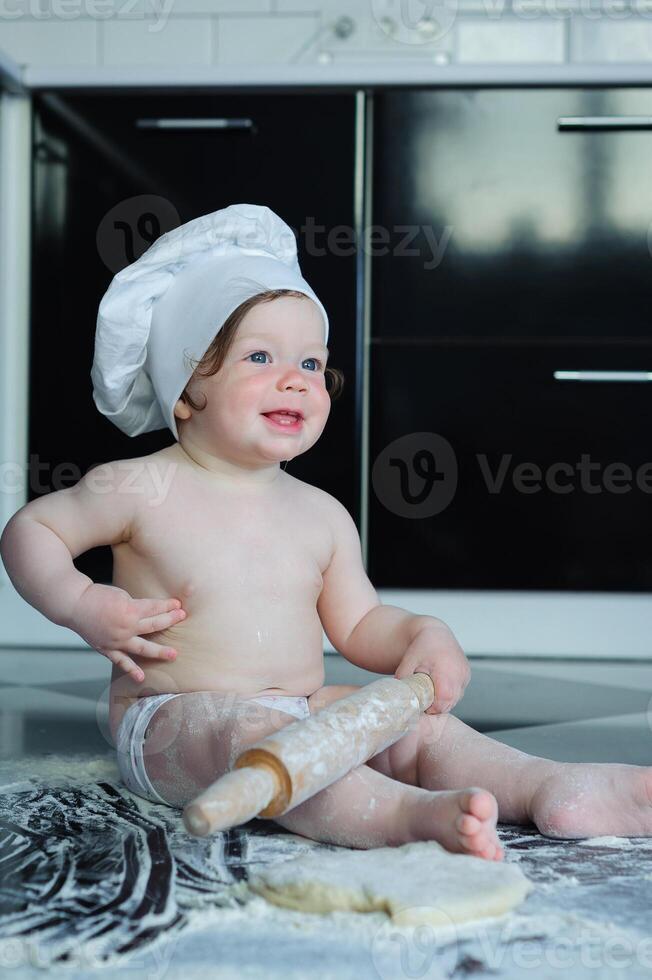 Little boy sitting on carpet in kitchen playing with cooking pots. Cute boy cooking in kitchen at home photo