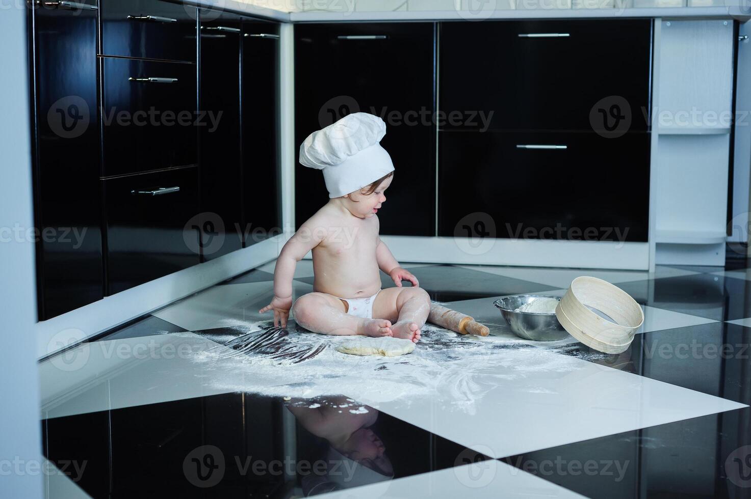 Little boy sitting on carpet in kitchen playing with cooking pots. Cute boy cooking in kitchen at home photo