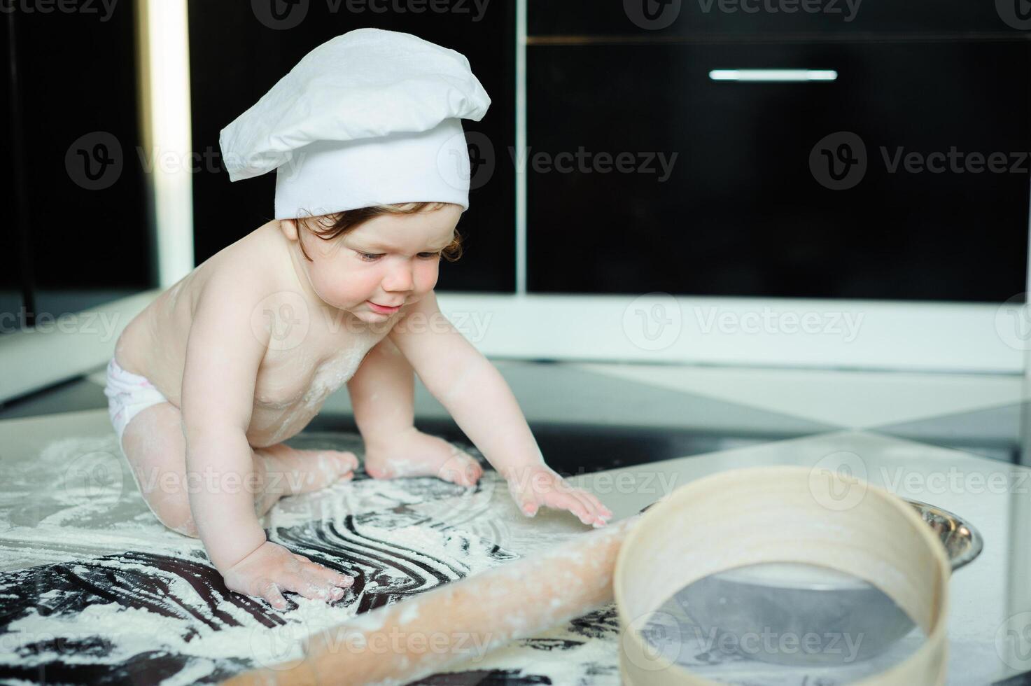 Little boy sitting on carpet in kitchen playing with cooking pots. Cute boy cooking in kitchen at home photo