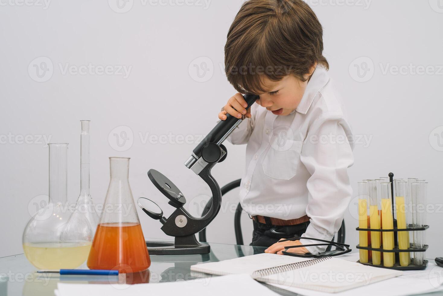 The boy with a microscope and various colorful flasks on a white background. A boy doing experiments in the laboratory. Explosion in the laboratory. Science and education. photo