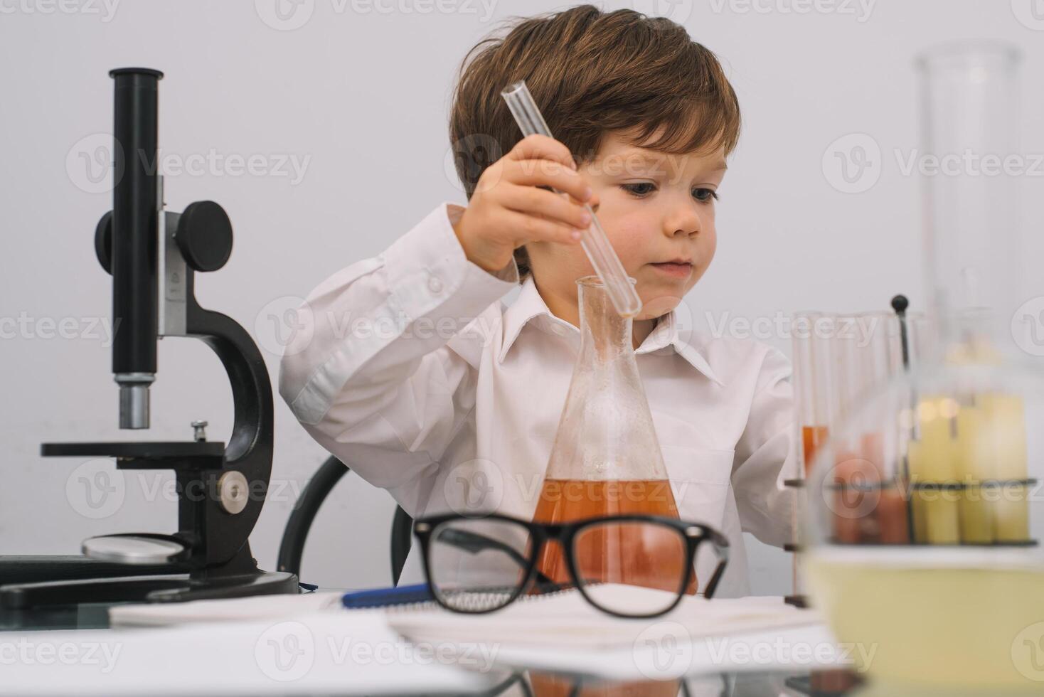 The boy with a microscope and various colorful flasks on a white background. A boy doing experiments in the laboratory. Explosion in the laboratory. Science and education photo