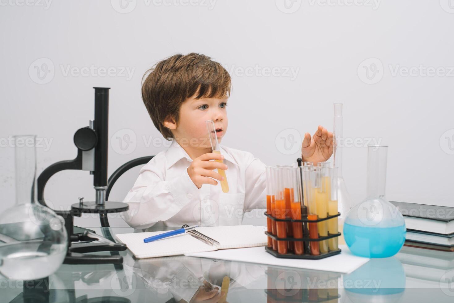 The boy with a microscope and various colorful flasks on a white background. A boy doing experiments in the laboratory. Explosion in the laboratory. Science and education photo