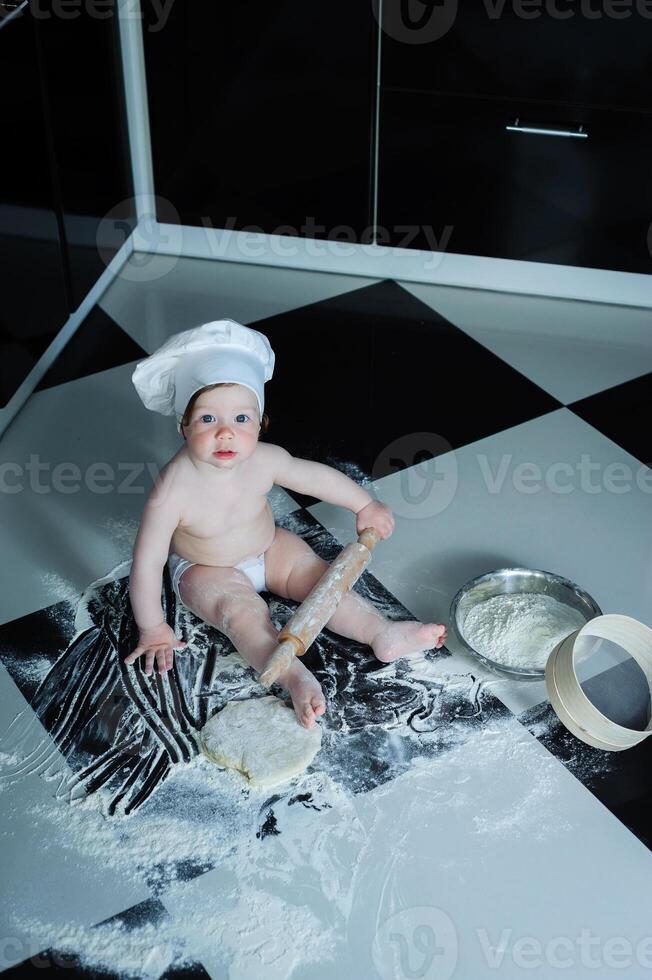 Little boy sitting on carpet in kitchen playing with cooking pots. Cute boy cooking in kitchen at home photo