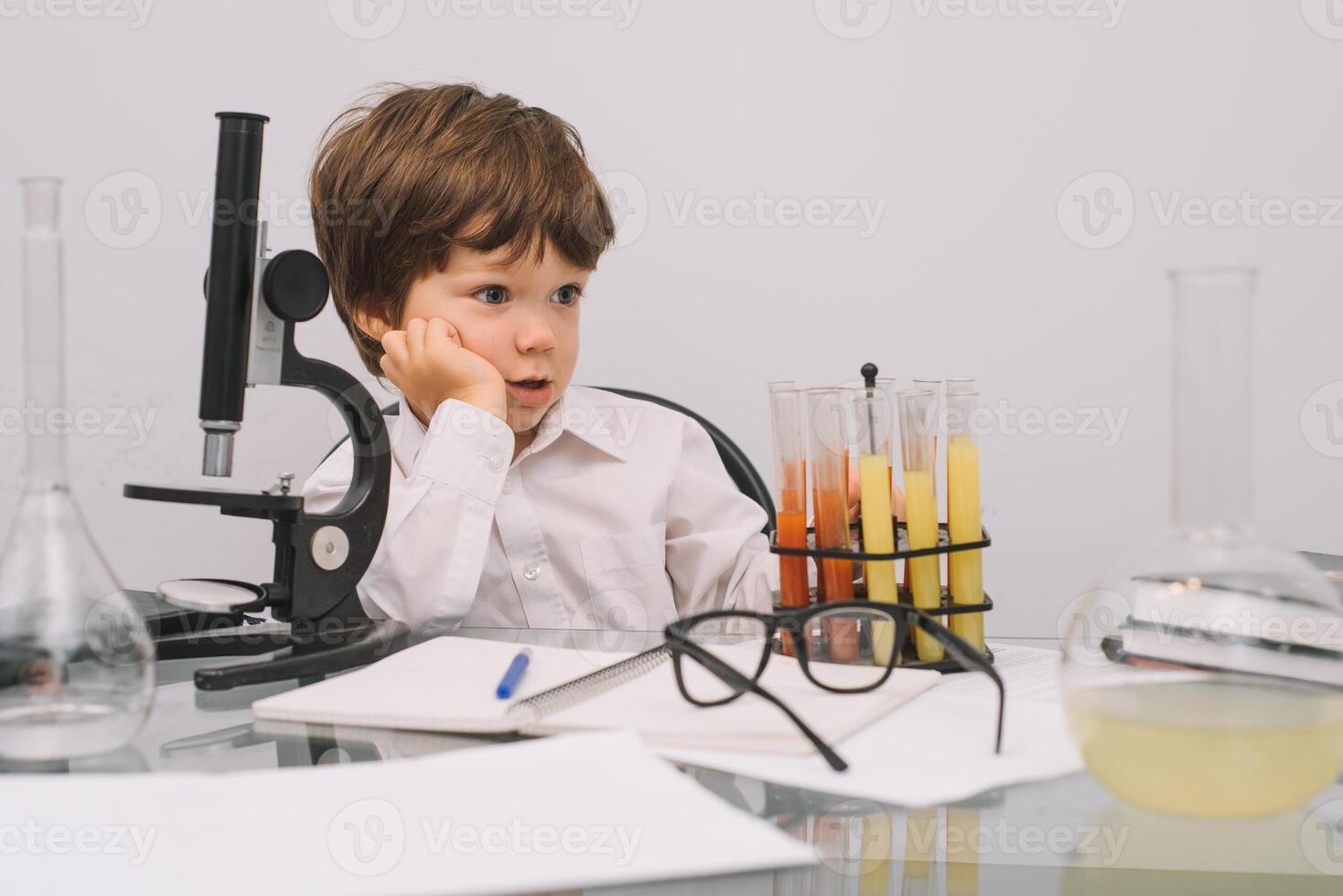 The boy with a microscope and various colorful flasks on a white background. A boy doing experiments in the laboratory. Explosion in the laboratory. Science and education photo