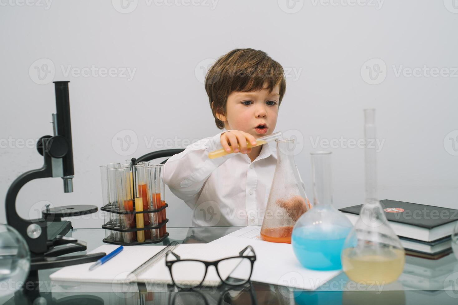 The boy with a microscope and various colorful flasks on a white background. A boy doing experiments in the laboratory. Explosion in the laboratory. Science and education photo