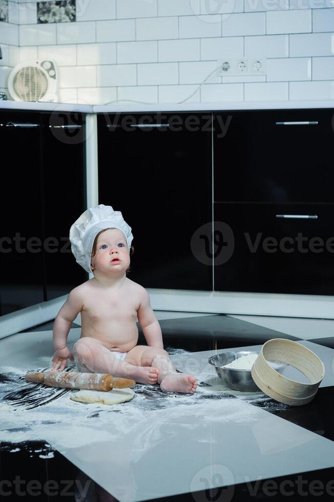 Little boy sitting on carpet in kitchen playing with cooking pots. Cute boy cooking in kitchen at home photo