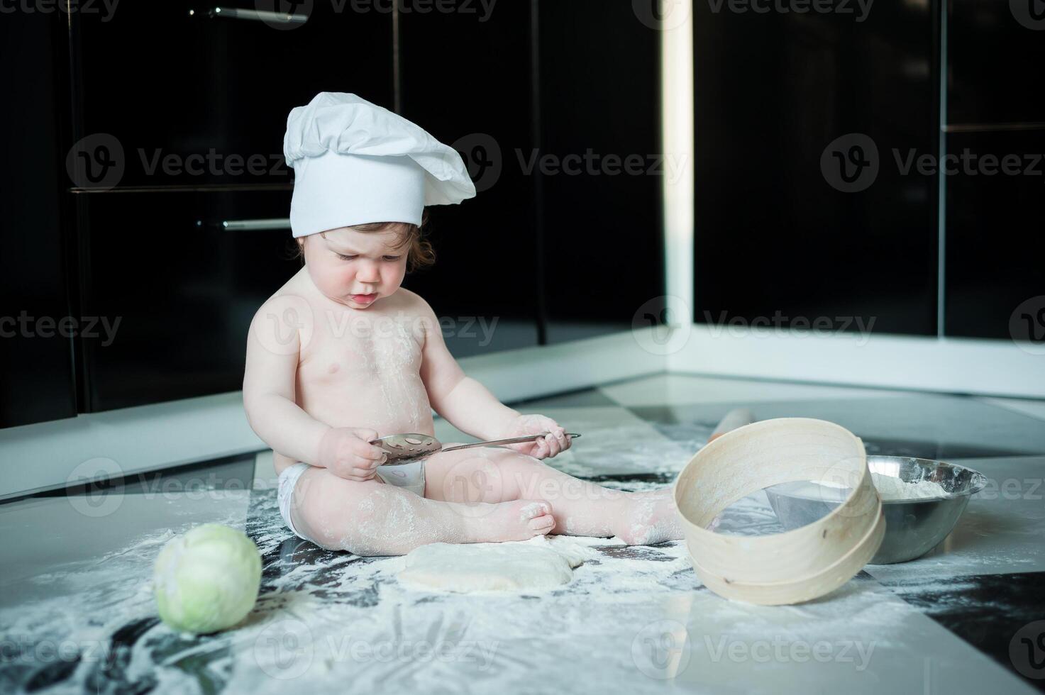 Little boy sitting on carpet in kitchen playing with cooking pots. Cute boy cooking in kitchen at home photo