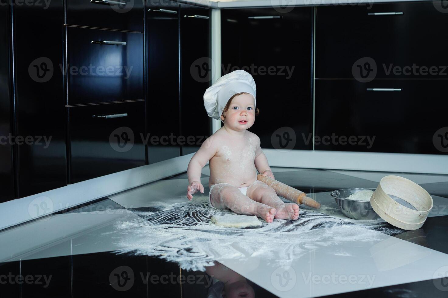 Little boy sitting on carpet in kitchen playing with cooking pots. Cute boy cooking in kitchen at home photo