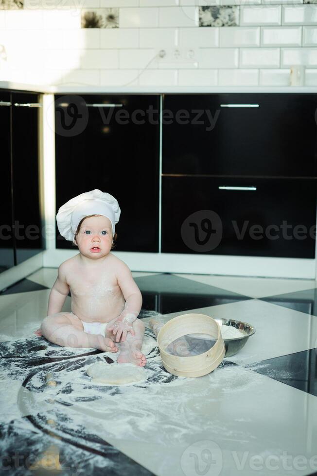 Little boy sitting on carpet in kitchen playing with cooking pots. Cute boy cooking in kitchen at home photo