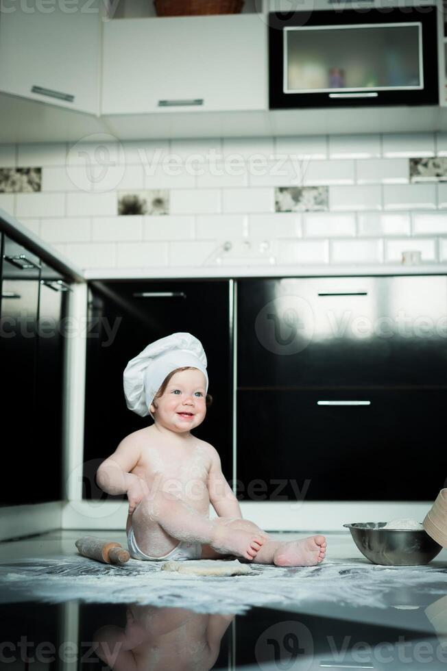 Little boy sitting on carpet in kitchen playing with cooking pots. Cute boy cooking in kitchen at home photo