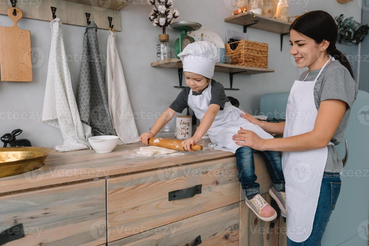 Young happy mom and her baby cook cookies at home in the kitchen. Christmas Homemade Gingerbread. cute boy with mother in white uniform and hat cooked chocolate cookies photo