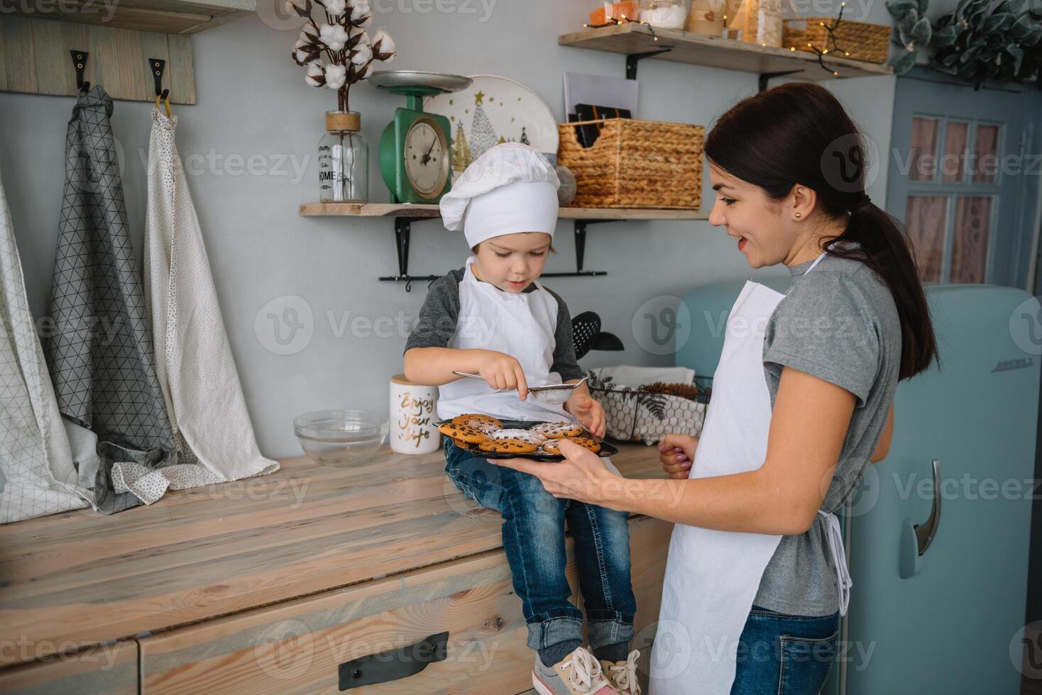 Young happy mom and her baby cook cookies at home in the kitchen. Christmas Homemade Gingerbread. cute boy with mother in white uniform and hat cooked chocolate cookies photo