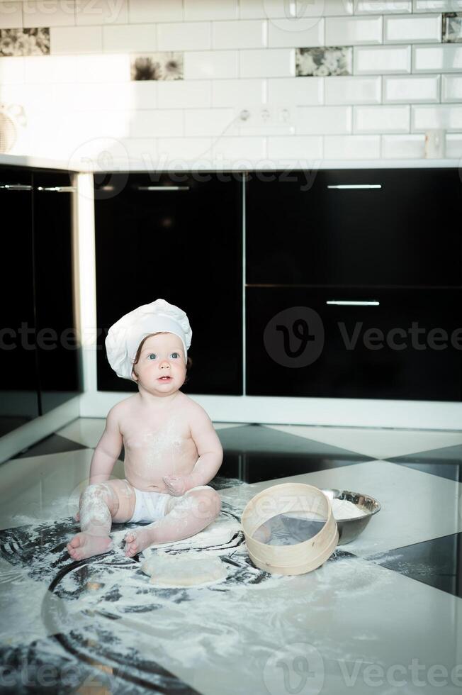 Little boy sitting on carpet in kitchen playing with cooking pots. Cute boy cooking in kitchen at home photo