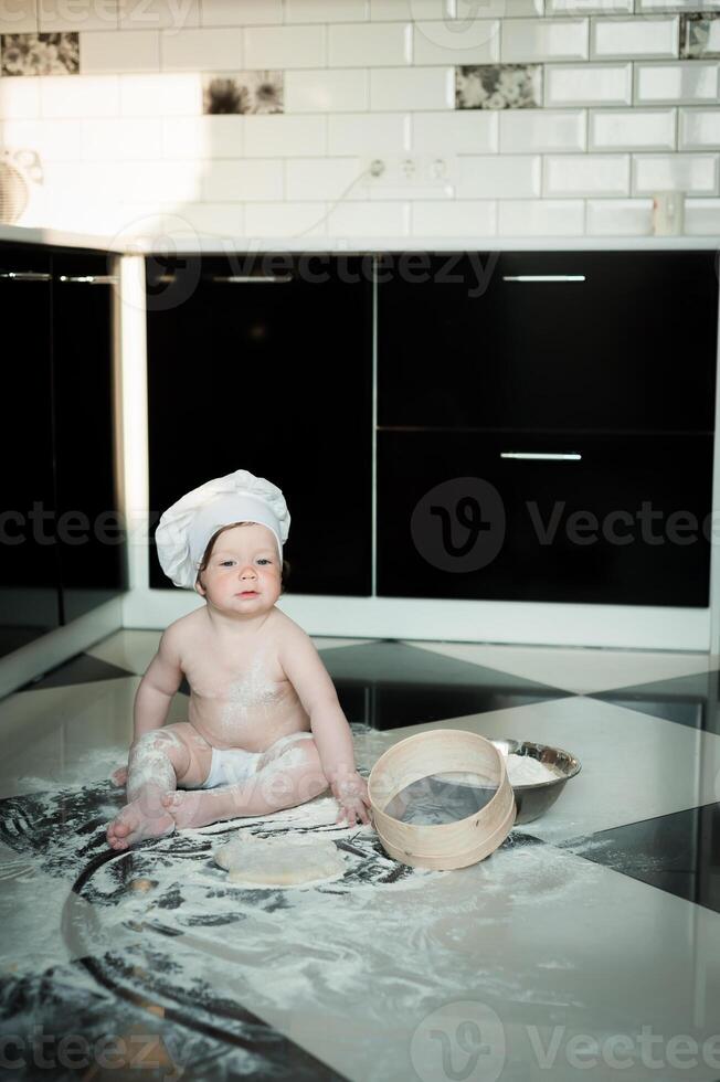 Little boy sitting on carpet in kitchen playing with cooking pots. Cute boy cooking in kitchen at home photo