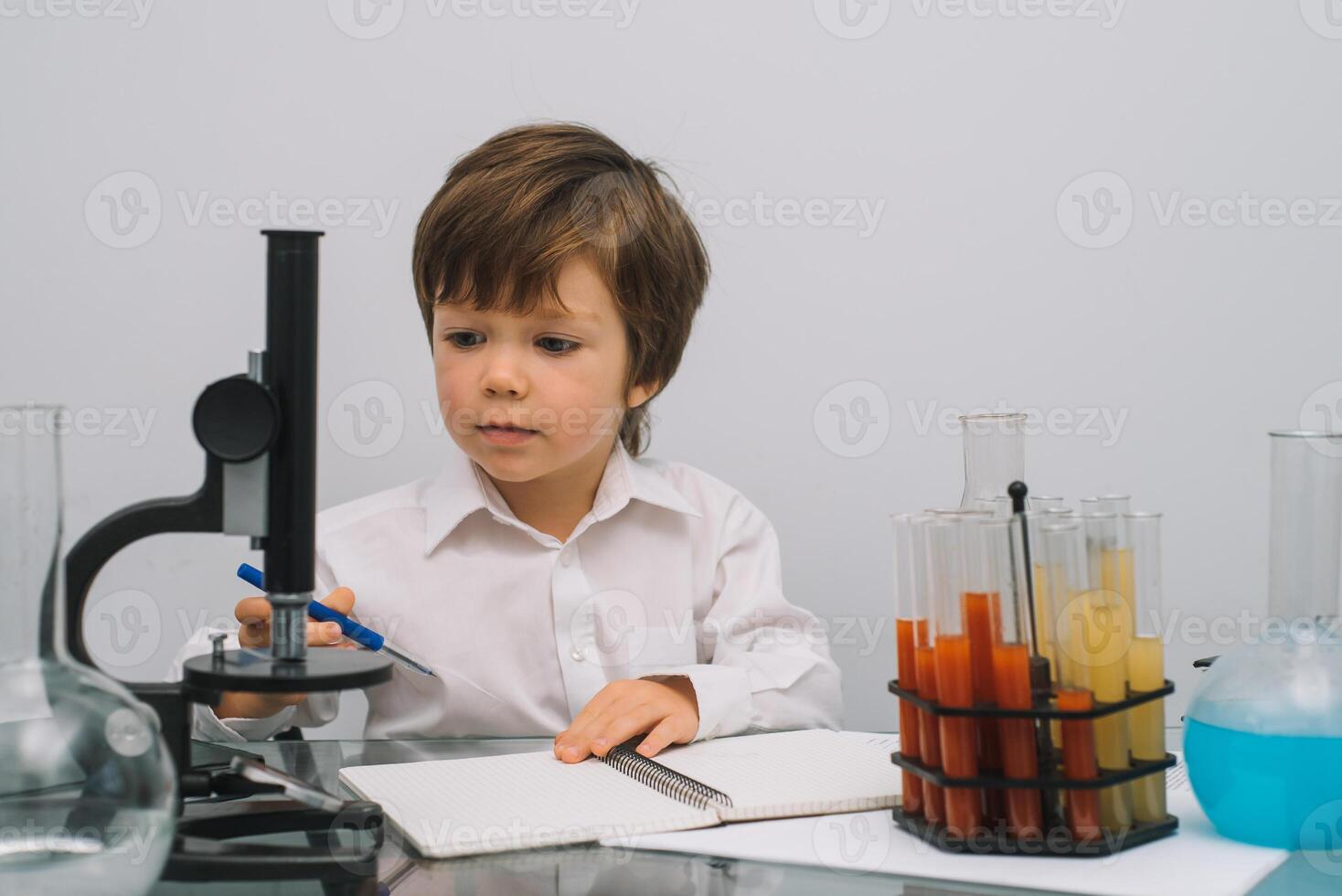 The boy with a microscope and various colorful flasks on a white background. A boy doing experiments in the laboratory. Explosion in the laboratory. Science and education photo