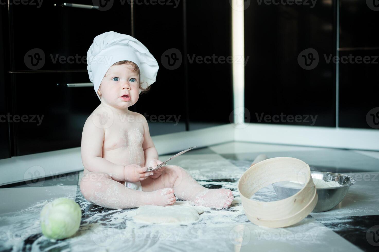 Little boy sitting on carpet in kitchen playing with cooking pots. Cute boy cooking in kitchen at home. photo