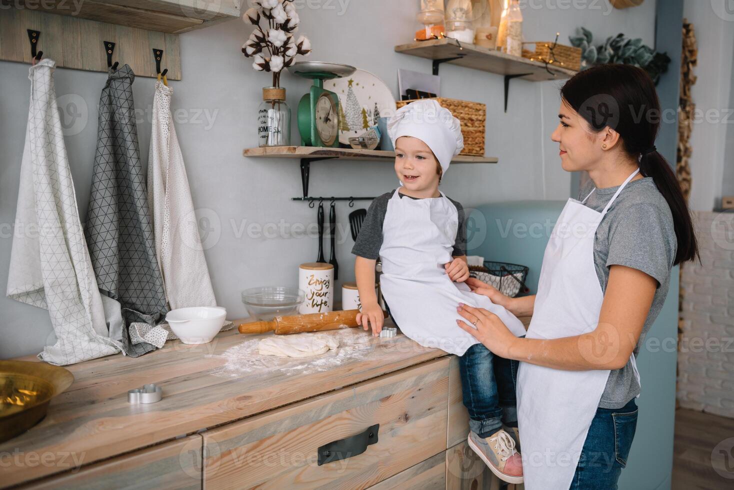 Young happy mom and her baby cook cookies at home in the kitchen. Christmas Homemade Gingerbread. cute boy with mother in white uniform and hat cooked chocolate cookies. photo