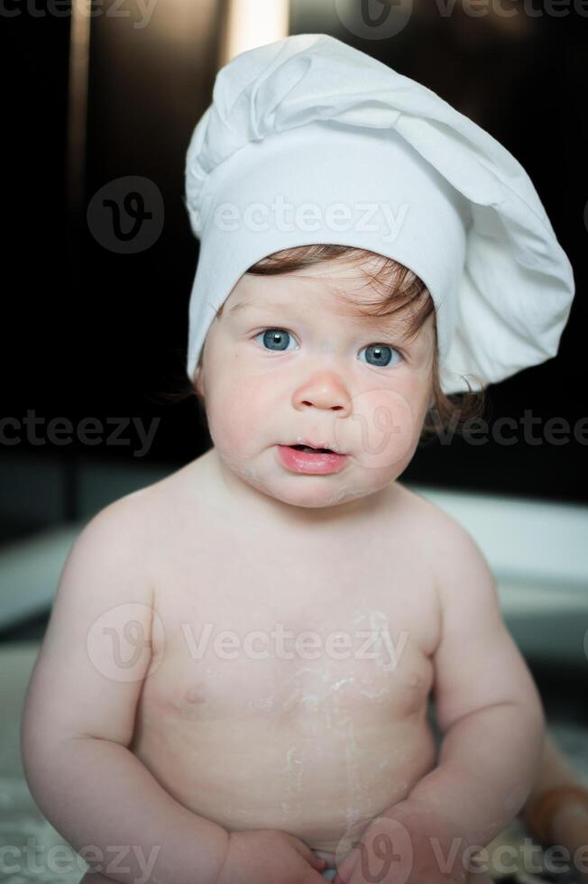 Little boy sitting on carpet in kitchen playing with cooking pots. Cute boy cooking in kitchen at home photo