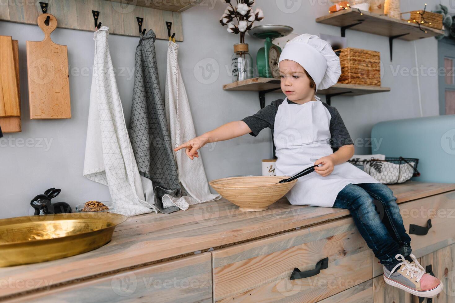 joven chico linda en el cocina cocinar cocinero en blanco uniforme y sombrero cerca mesa. Navidad hecho en casa pan de jengibre. el chico cocido el chocolate galletas. foto