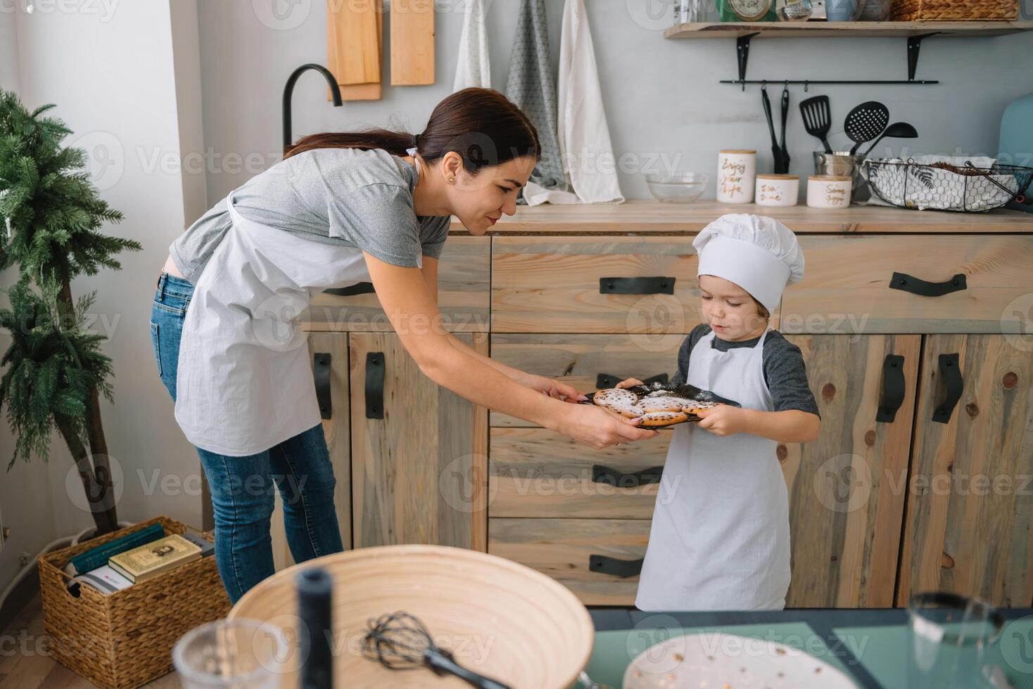 Young happy mom and her baby cook cookies at home in the kitchen. Christmas Homemade Gingerbread. cute boy with mother in white uniform and hat cooked chocolate cookies photo