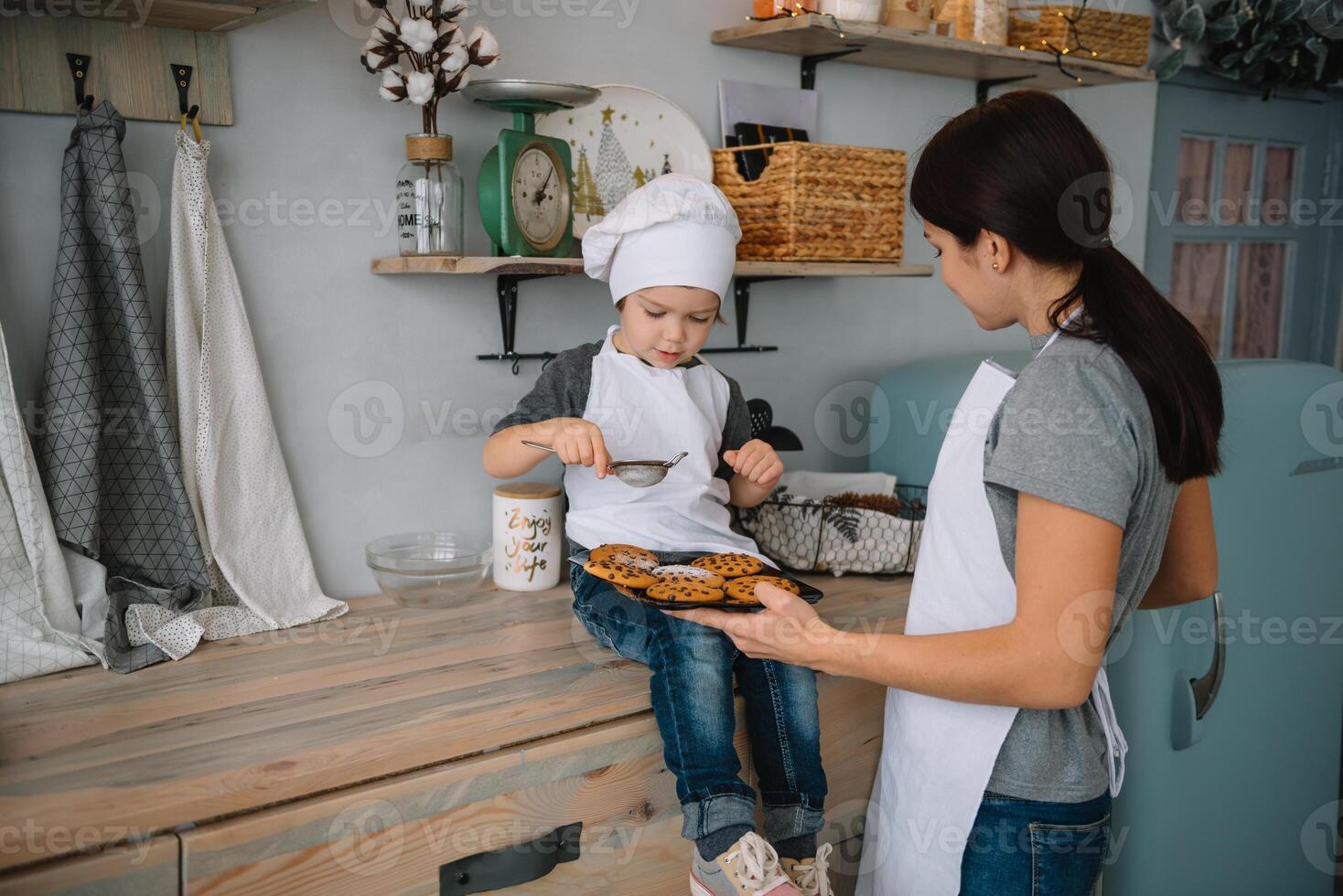 Young happy mom and her baby cook cookies at home in the kitchen. Christmas Homemade Gingerbread. cute boy with mother in white uniform and hat cooked chocolate cookies photo