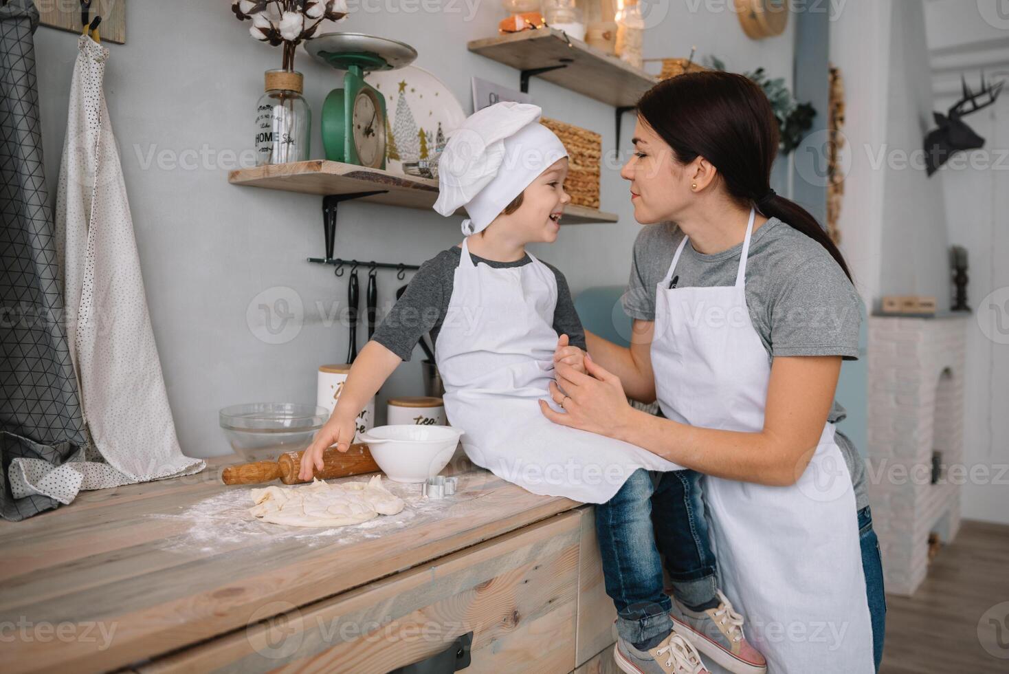Young happy mom and her baby cook cookies at home in the kitchen. Christmas Homemade Gingerbread. cute boy with mother in white uniform and hat cooked chocolate cookies. photo