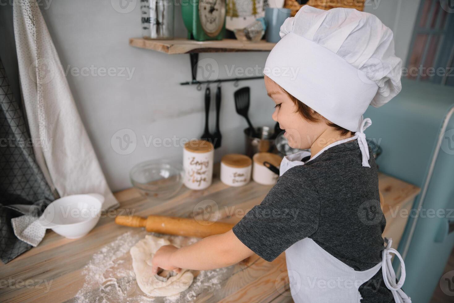 Young boy cute on the kitchen cook chef in white uniform and hat near table. Christmas homemade gingerbread. the boy cooked the chocolate cookies. photo