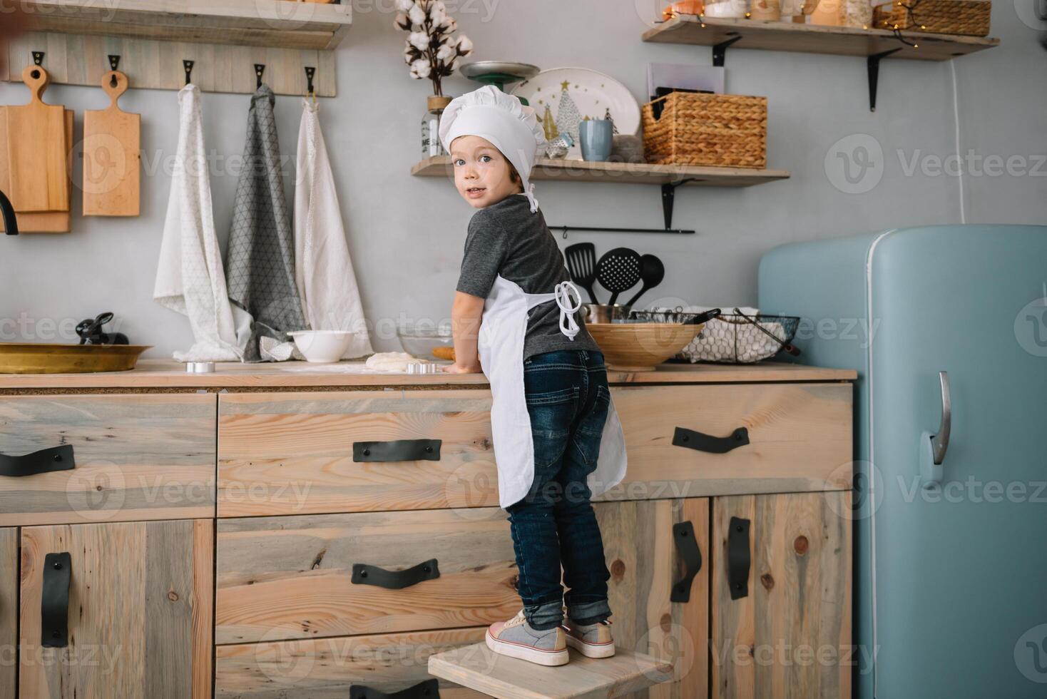 Young happy mom and her baby cook cookies at home in the kitchen. Christmas Homemade Gingerbread. cute boy with mother in white uniform and hat cooked chocolate cookies. photo