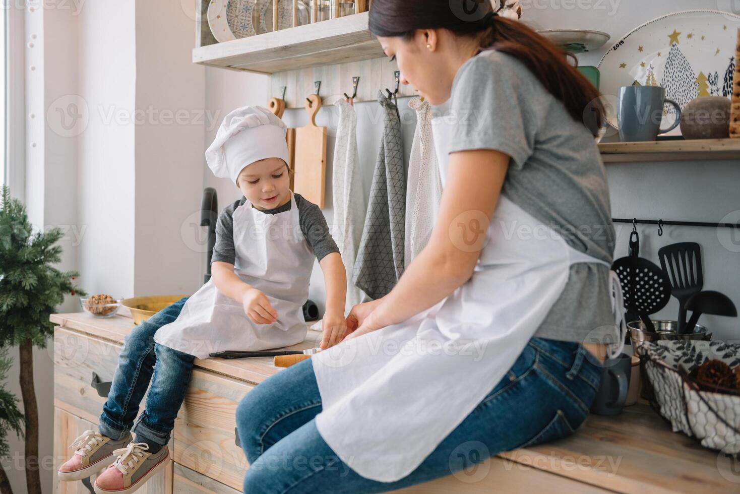 Young happy mom and her baby cook cookies at home in the kitchen. Christmas Homemade Gingerbread. cute boy with mother in white uniform and hat cooked chocolate cookies photo