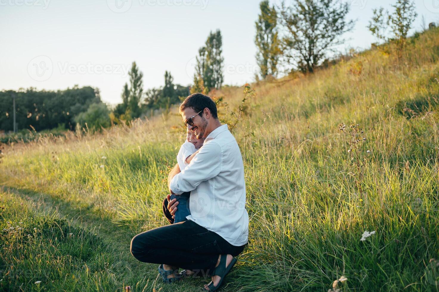 Handsome dad with his little cute son are having fun and playing on green grassy lawn. Happy family concept. Beauty nature scene with family outdoor lifestyle. family resting together. Fathers day. photo