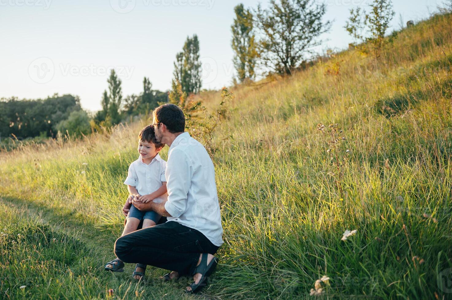 Handsome dad with his little cute son are having fun and playing on green grassy lawn. Happy family concept. Beauty nature scene with family outdoor lifestyle. family resting together. Fathers day. photo