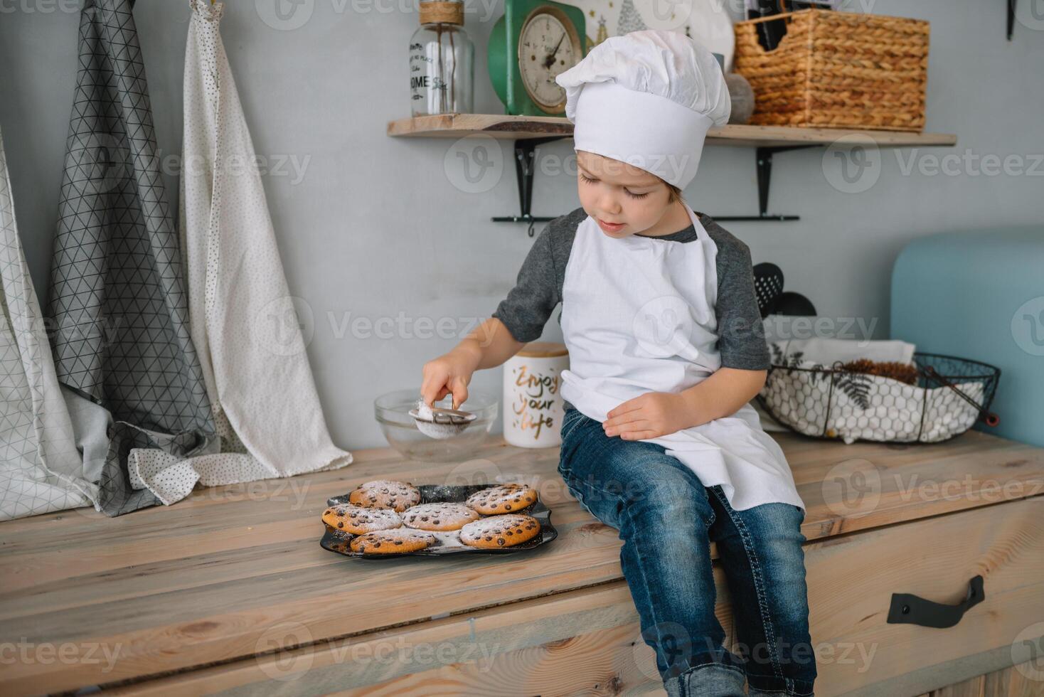 joven contento mamá y su bebé cocinar galletas a hogar en el cocina. Navidad hecho en casa pan de jengibre. linda chico con madre en blanco uniforme y sombrero cocido chocolate galletas foto