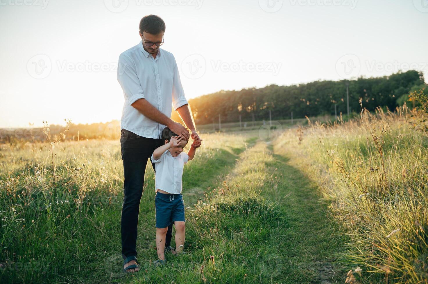 Handsome dad with his little cute son are having fun and playing on green grassy lawn. Happy family concept. Beauty nature scene with family outdoor lifestyle. family resting together. Fathers day photo