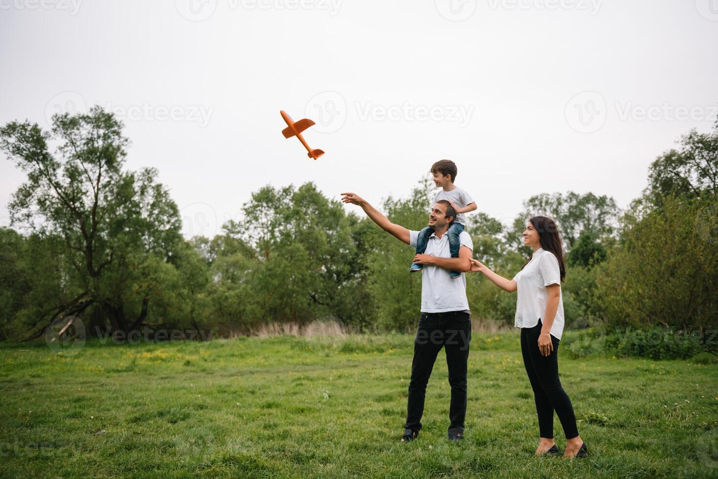 Father, mother and son playing with toy airplane in the park. friendly family. People having fun outdoors. Picture made on the background of the park and blue sky. concept of a happy family photo