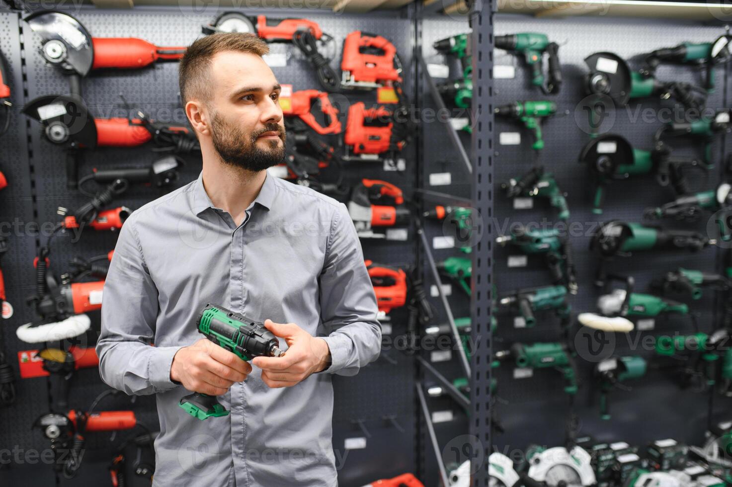 a man in a hardware store chooses a new screwdriver next to a showcase of power tools photo