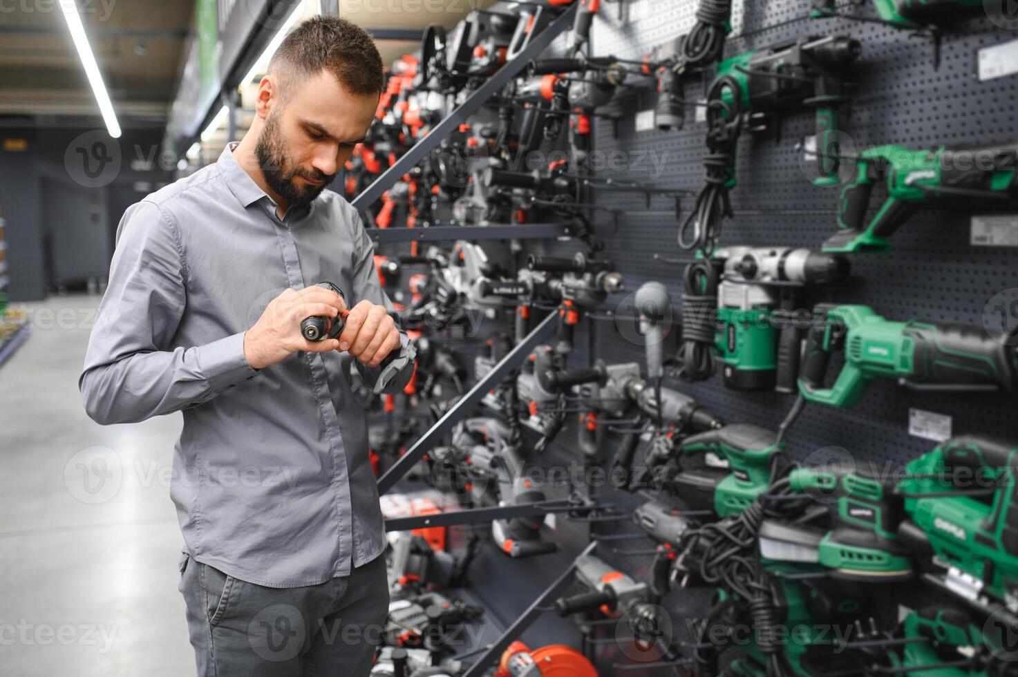 a man in a hardware store chooses a new screwdriver next to a showcase of power tools photo