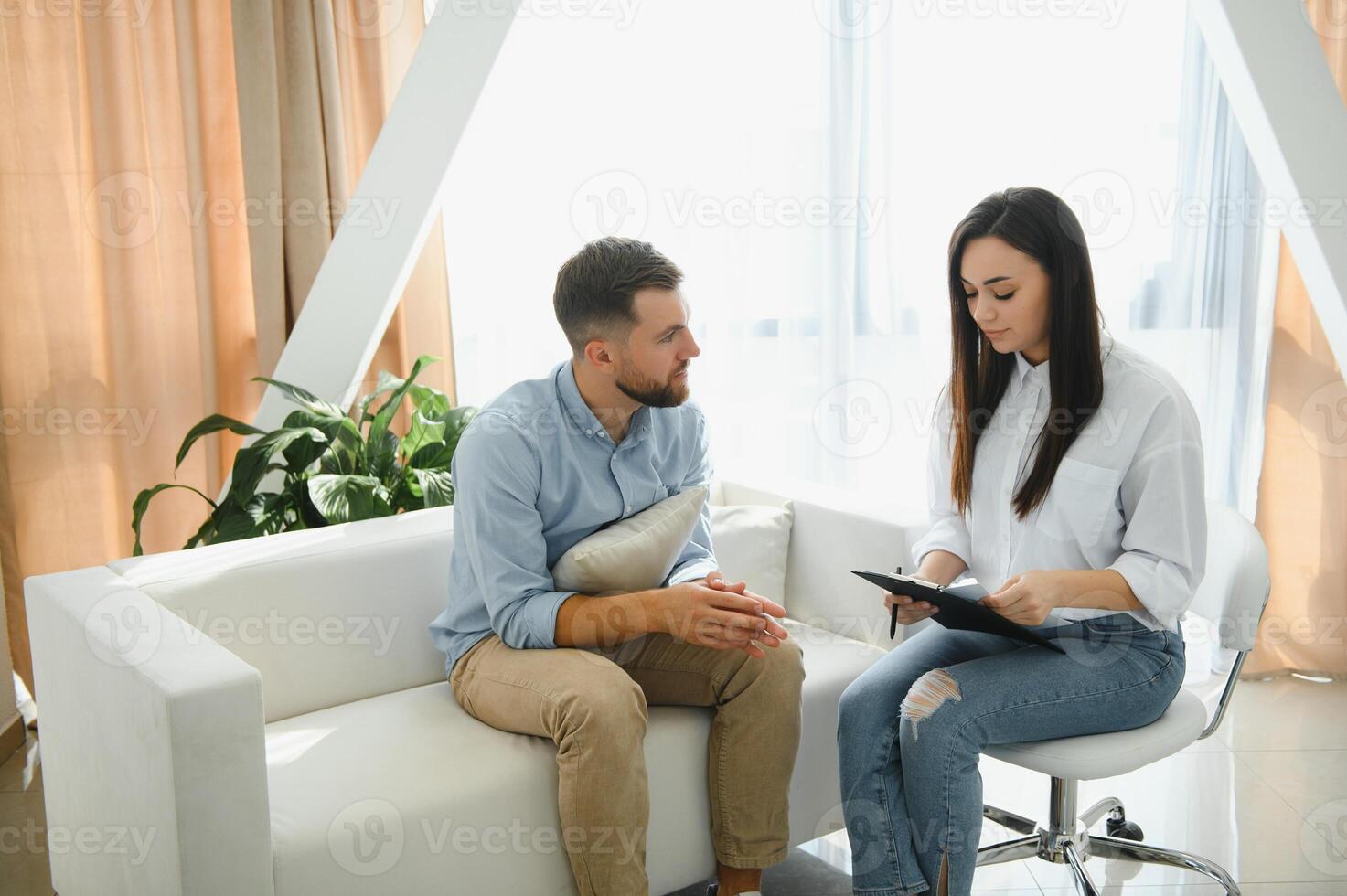 Psychologist talking with patient on therapy session. Depressed man speaking to a therapist while she is taking notes photo