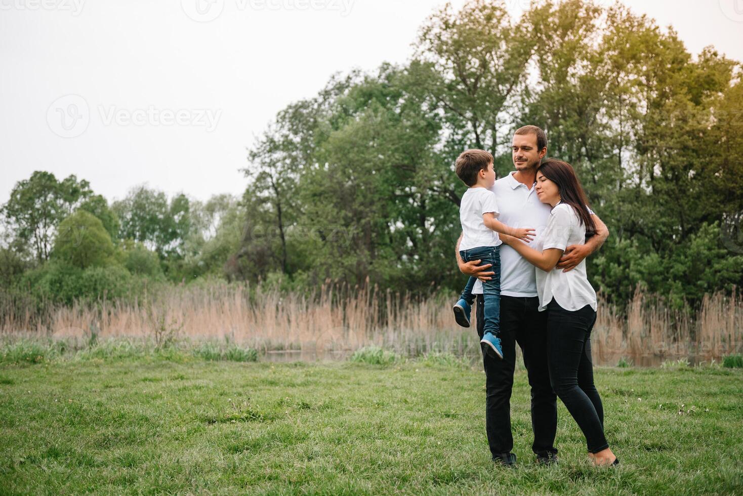 contento familia madre padre y niño hijo en naturaleza en puesta de sol. mamá, papá y niño riendo y abrazando, disfrutando naturaleza afuera. soleado día, bueno humor. concepto de un contento familia. foto