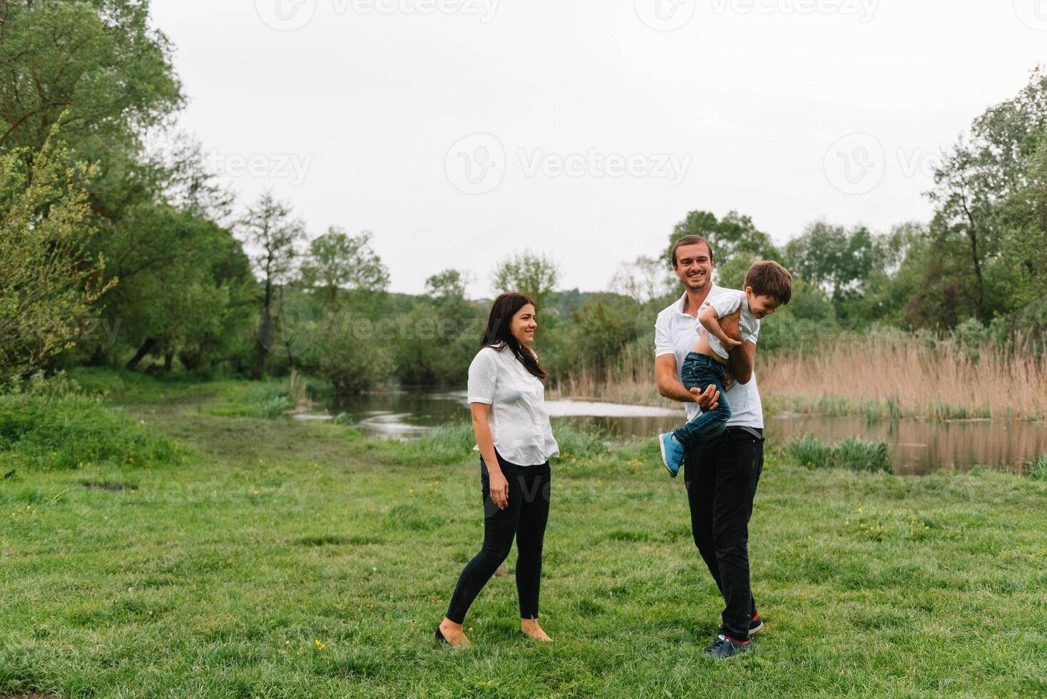 contento familia madre padre y niño hijo en naturaleza en puesta de sol. mamá, papá y niño riendo y abrazando, disfrutando naturaleza afuera. soleado día, bueno humor. concepto de un contento familia foto