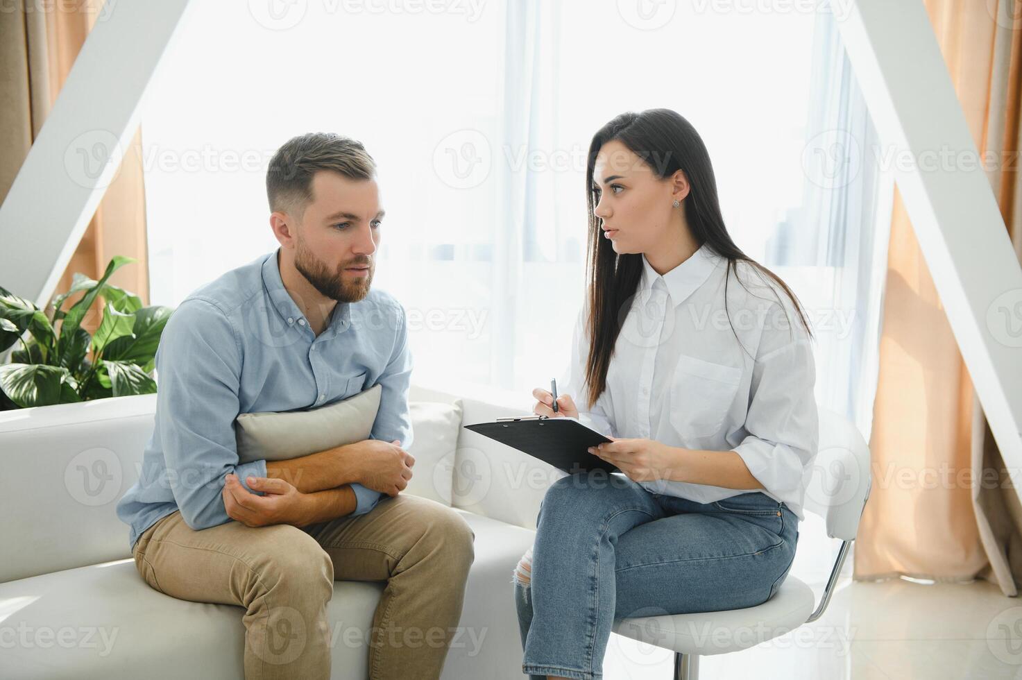 Session with a psychologist, psychotherapist. Young depressed male patient and professional female doctor with note pad. Lifestyle. Mental health care. photo