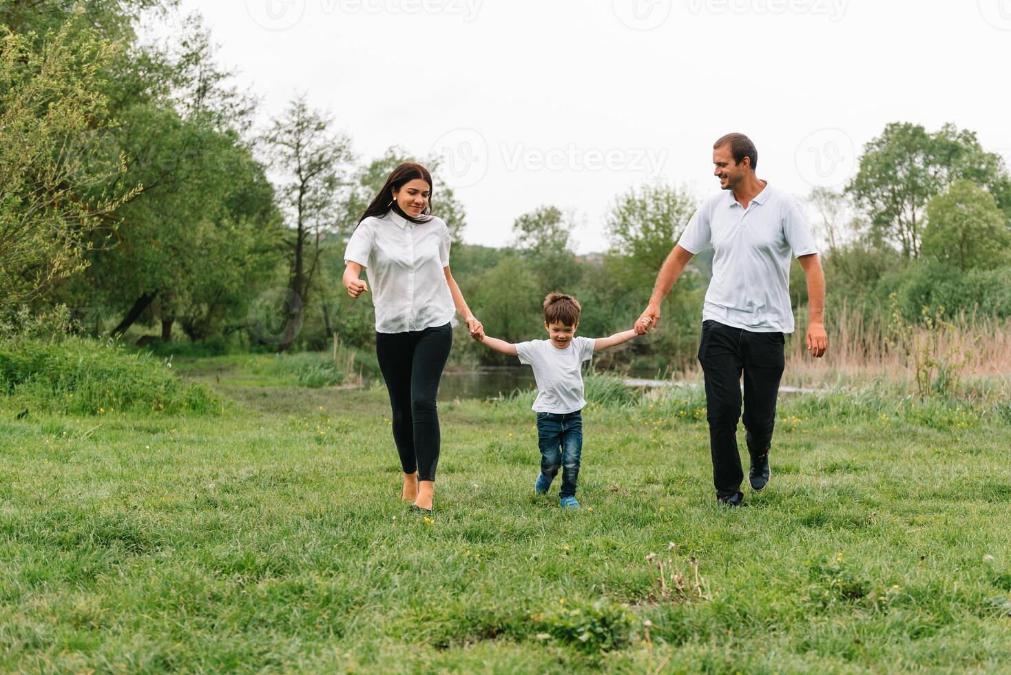 contento familia madre padre y niño hijo en naturaleza en puesta de sol. mamá, papá y niño riendo y abrazando, disfrutando naturaleza afuera. soleado día, bueno humor. concepto de un contento familia. foto