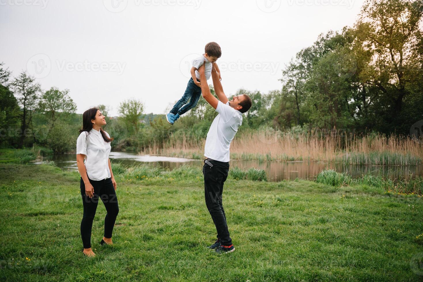 contento familia madre padre y niño hijo en naturaleza en puesta de sol. mamá, papá y niño riendo y abrazando, disfrutando naturaleza afuera. soleado día, bueno humor. concepto de un contento familia foto